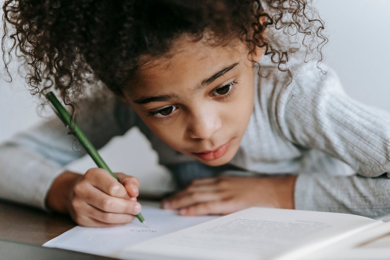 Black girl concentrating while writing in a workbook at a table.