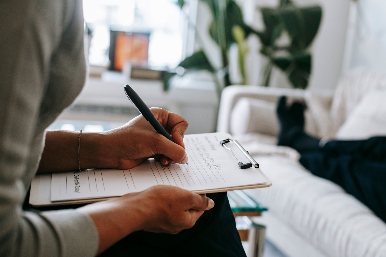 Psychologist writing notes on a clipboard during a clinical appointment.