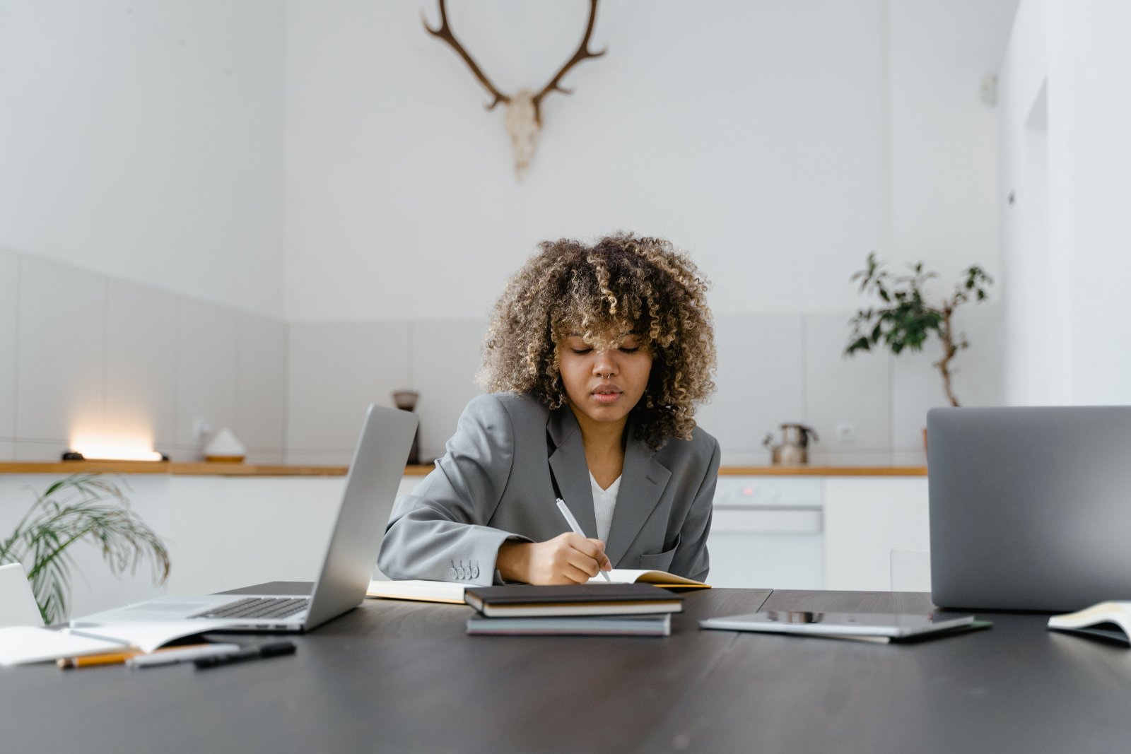 Black woman writing in a planner while working at a table with laptops and notebooks.