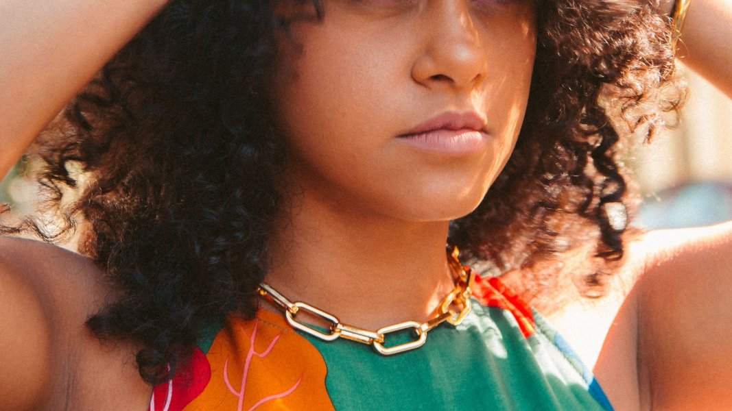A Black girl examining her hair in a mirror, looking concerned.