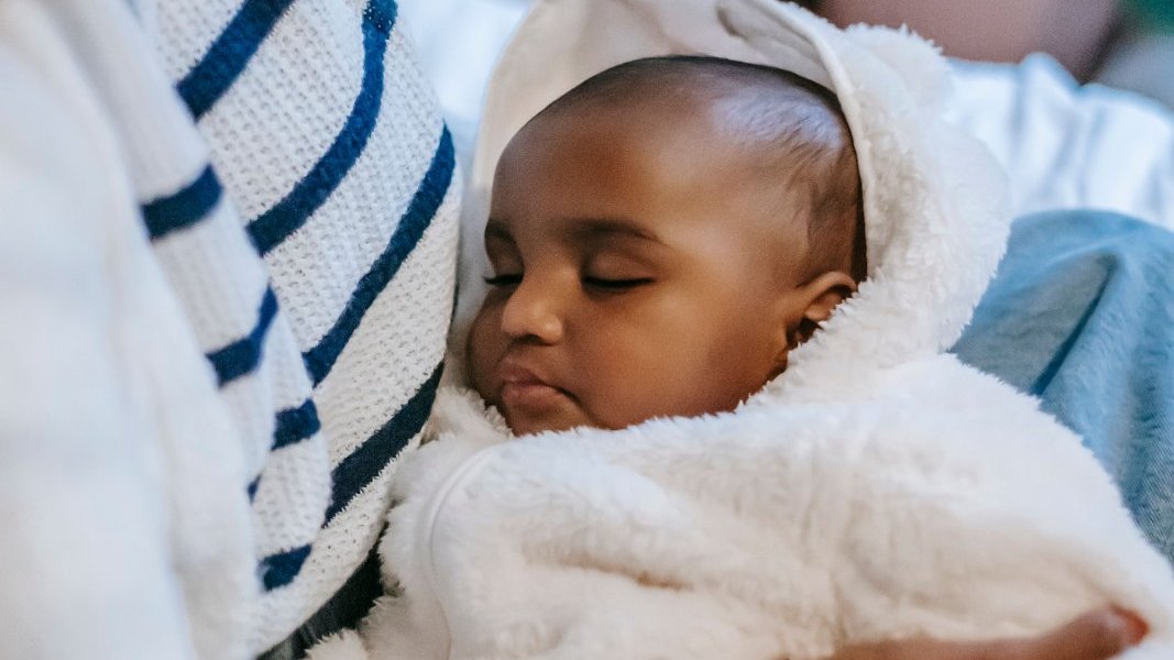 A Black mother holding her baby, looking thoughtful.